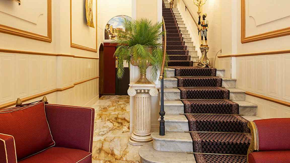 Tyylikäs eteinen, jossa punaisia huonekaluja ja kuvioidulla matolla varustettu portaikko. (Tekoälyn luoma teksti)