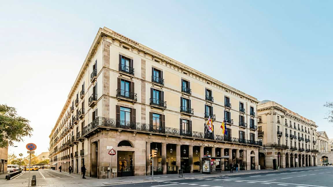 Kadun kulma, jossa on klassista tyyliä edustava rakennus, jossa on useita kerroksia, kaaria ja koristeellisia parvekkeita. (Tekoälyn luoma teksti)