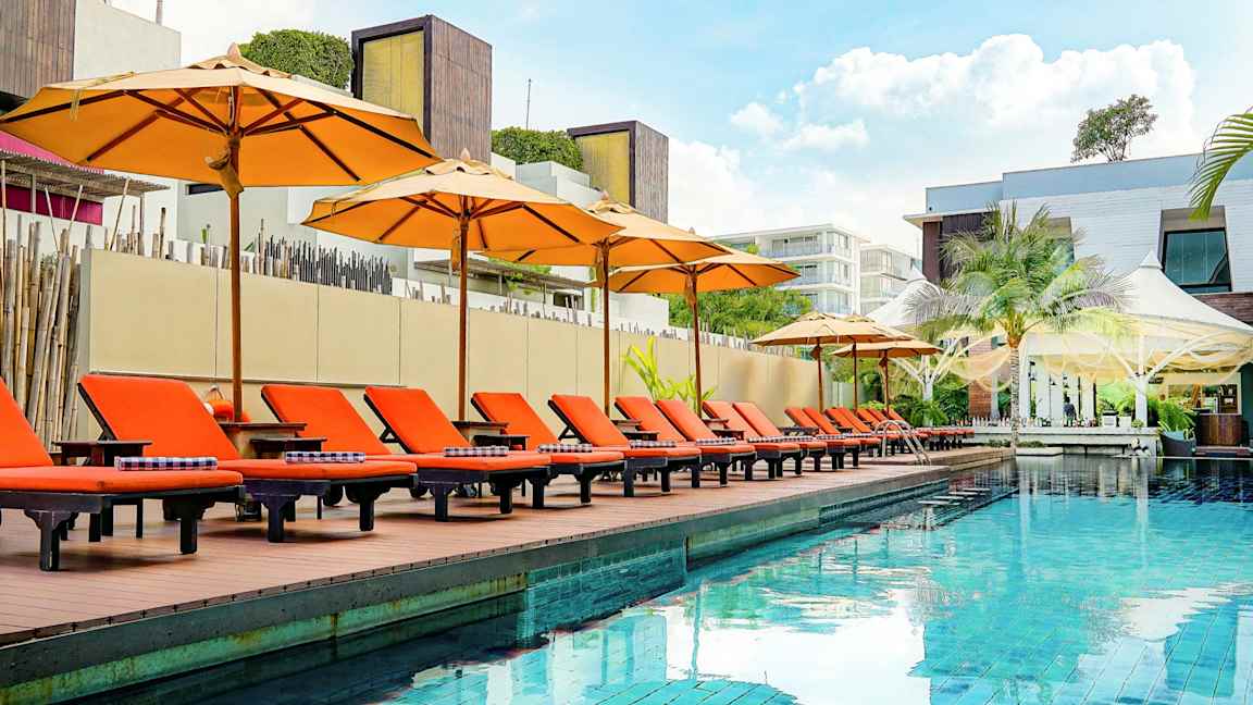 Ulkouima-allas, jonka reunalla on oransseja aurinkotuoleja ja varjoja, ympäröity modernilla arkkitehtuurilla. (Tekoälyn luoma teksti)