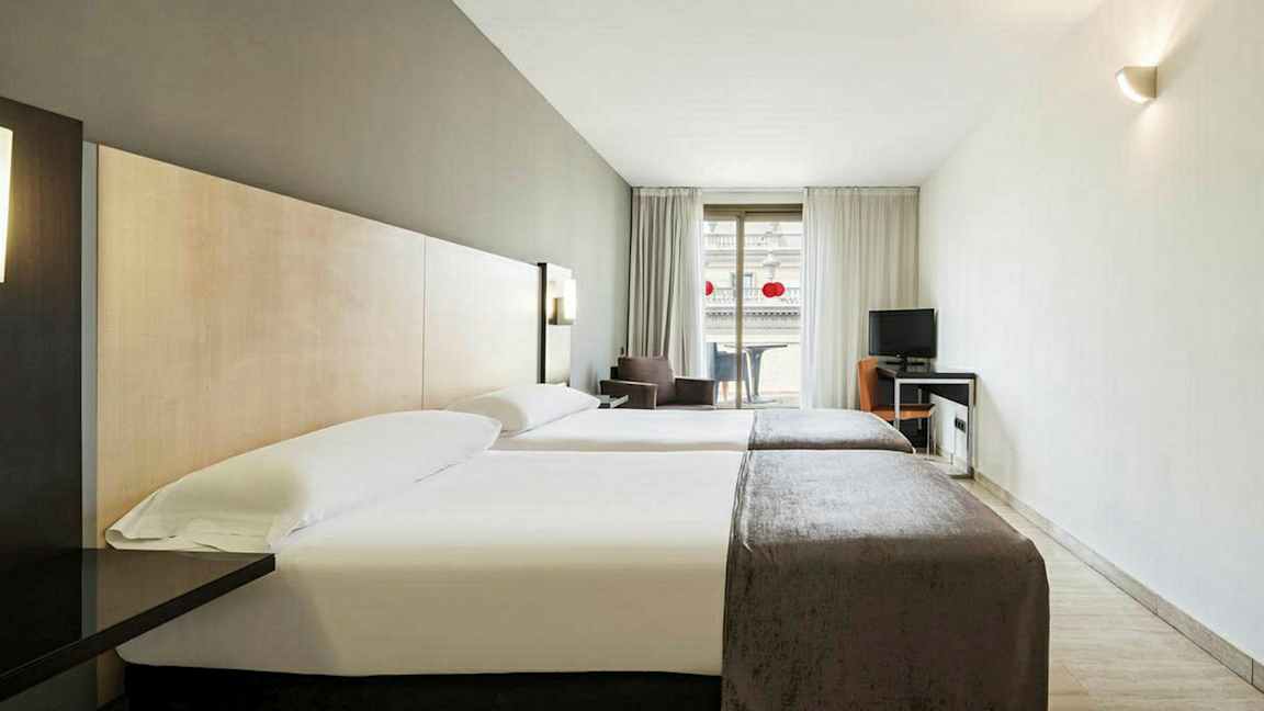 Hotellihuone, jossa on kaksi yhden hengen sänkyä ja työpöytä parvekkeen vieressä. (Tekoälyn luoma teksti)