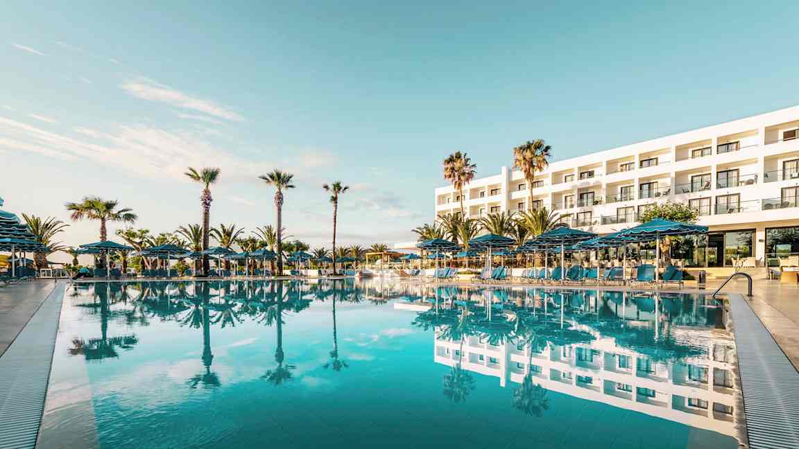 Hotellin ulkopuoli, jossa suuri uima-allas edessä ja ympäröivät palmut. (Tekoälyn luoma teksti)