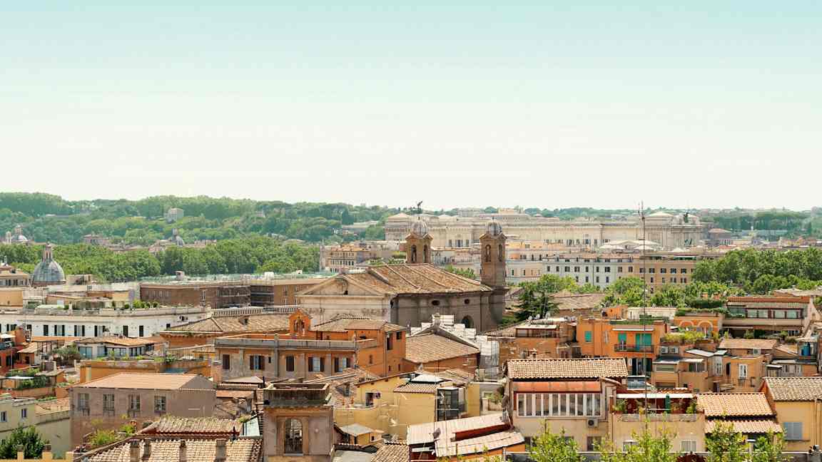 Näkymä kaupunkiin, jossa on monia rakennuksia, kaksi kirkontornia ja vihreä kasvillisuus taustalla. (Tekoälyn luoma teksti)