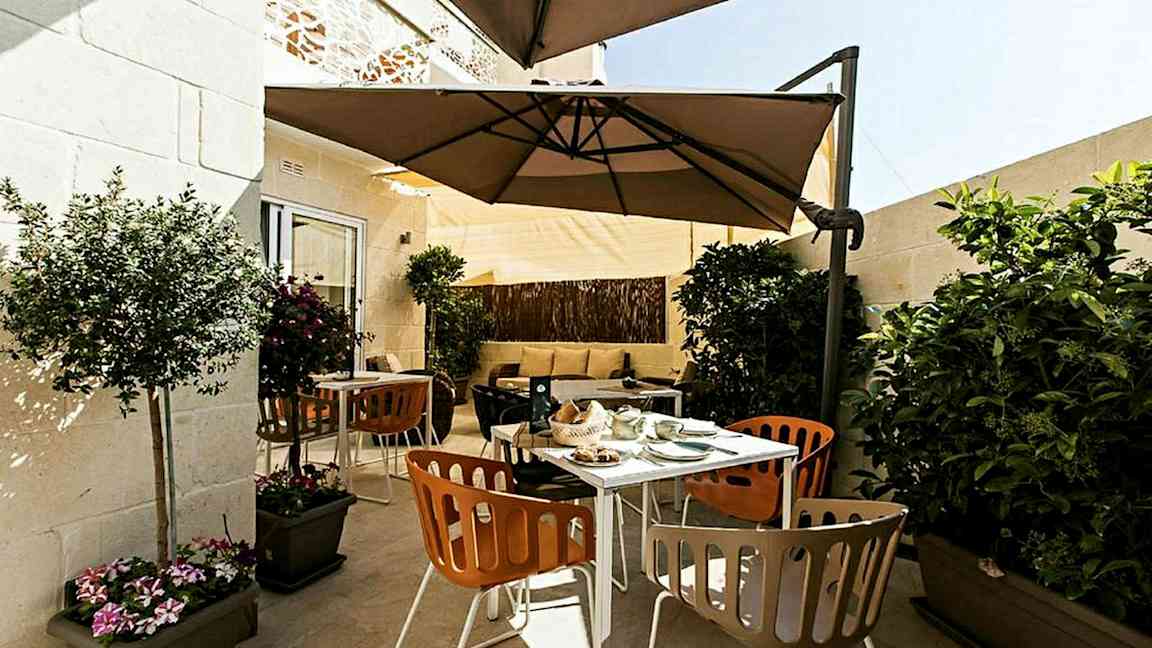 Terassi, jossa on ulkokalusteita, varjoja ja kasveja. (Tekoälyn luoma teksti)