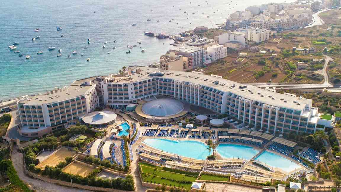 Ilmakuva hotellialueesta, jossa on uima-altaita, vihreitä alueita ja merinäköala. (Tekoälyn luoma teksti)