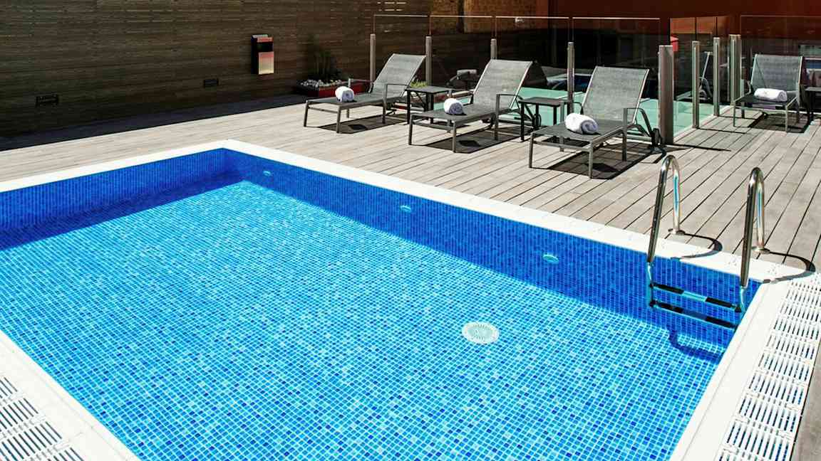 Sininen mosaiikkiallas, jossa on aurinkotuoleja puulattialla. (Tekoälyn luoma teksti)