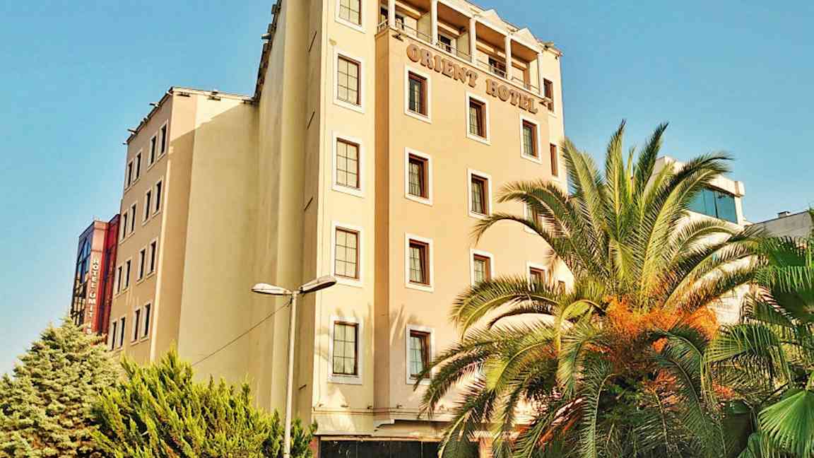 Monikerroksinen hotellirakennus. Rakennuksen edessä on palmuja ja vihreitä puita. (Tekoälyn luoma teksti)