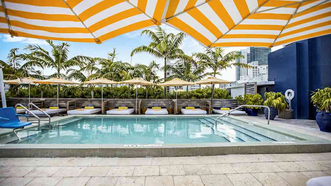 Uima-allasalue, jossa on aurinkotuoleja, aurinkovarjoja ja palmuja taustalla. (Tekoälyn luoma teksti)