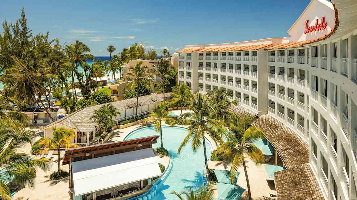 Hotelli, jossa on uima-allas, ympäröiviä palmuja ja lähellä sijaitseva ranta. (Tekoälyn luoma teksti)