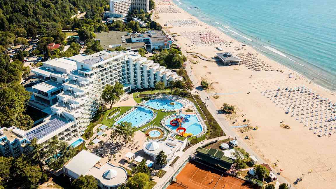 Ilmakuva hotellista, jossa on allasalue, viheralueita ja ranta. (Tekoälyn luoma teksti)