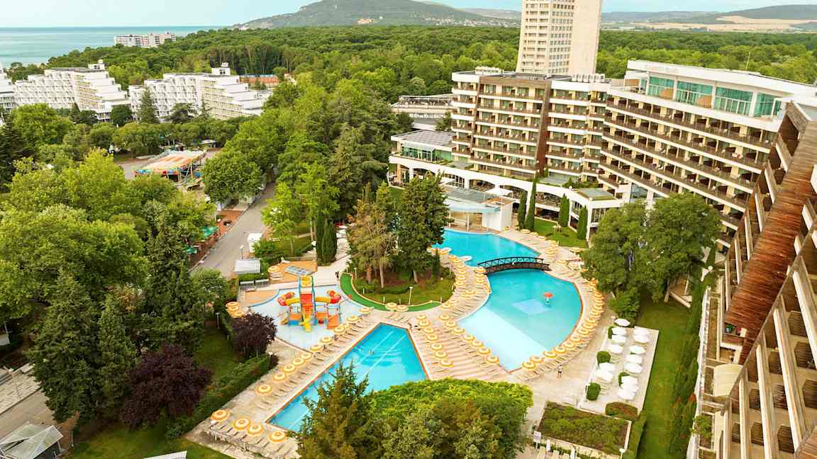 Näkymä hotellialueelle, jossa on uima-altaita, aurinkotuoleja ja ympäröiviä puita. (Tekoälyn luoma teksti)