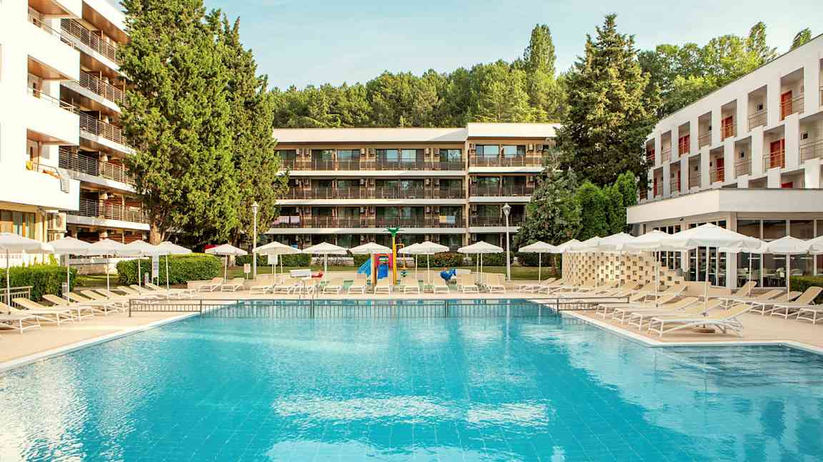 Ulkouima-allas, jonka ympärillä aurinkotuoleja ja varjoja, ympäröitynä modernilla rakennuksilla ja vehreydellä. (Tekoälyn luoma teksti)