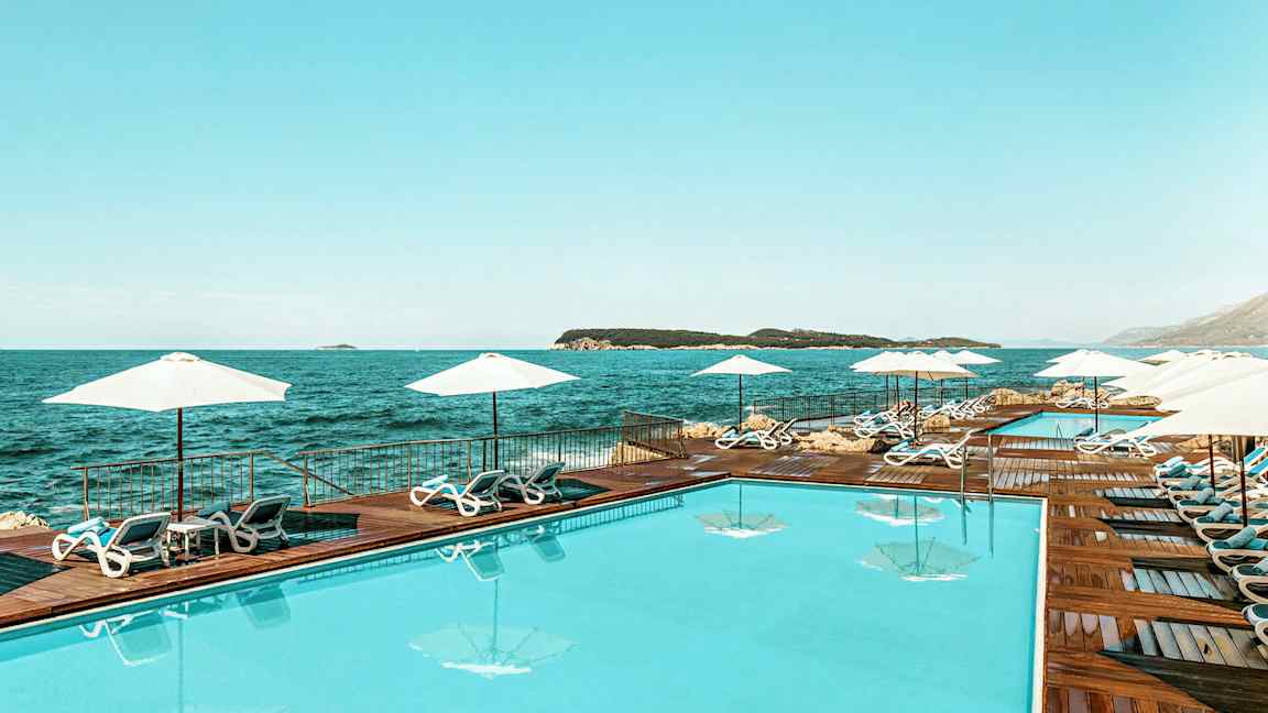 Uima-allas meren äärellä, jonka ympärillä aurinkotuoleja ja aurinkovarjoja. (Tekoälyn luoma teksti)