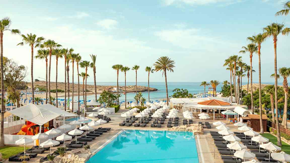 Kuva altaasta, jossa on aurinkotuoleja, aurinko- ja palmuja rannalla. (Tekoälyn luoma teksti)