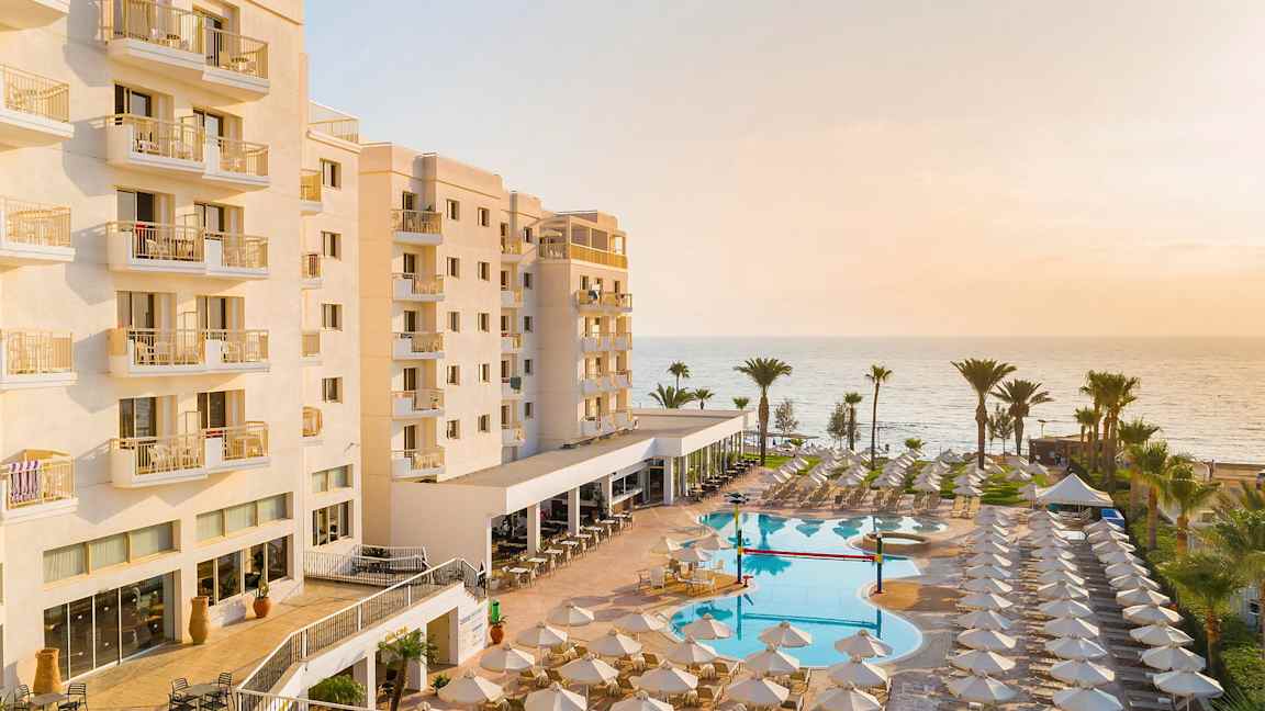 Hotellirakennus, jossa parvekkeet, uima-allas ja aurinkotuoleja rannan äärellä. (Tekoälyn luoma teksti)