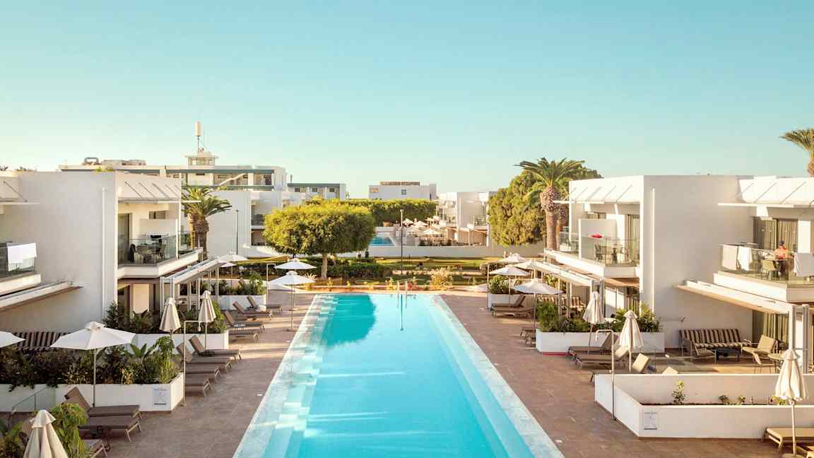 Ulkouima-allas, jota ympäröivät modernit valkoiset rakennukset, joissa on parvekkeita ja aurinkotuoleja varjojen alla. (Tekoälyn luoma teksti)