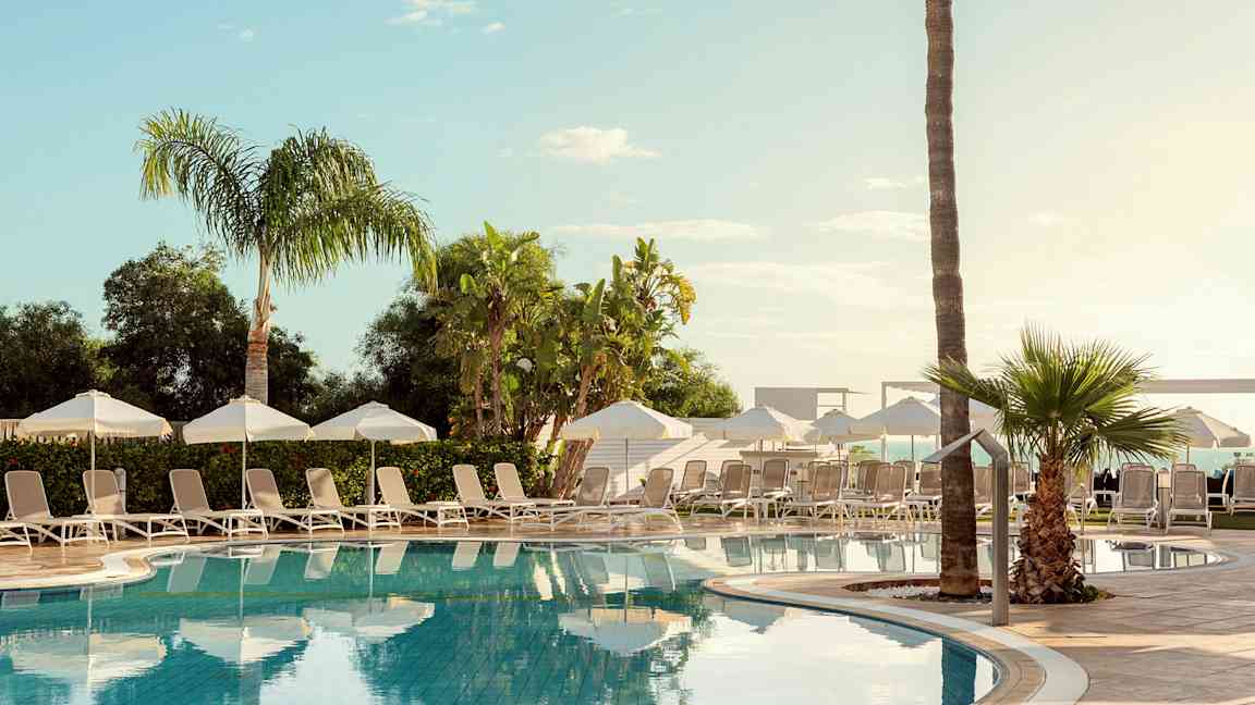 Ulkoallas, jonka ympärillä aurinkotuoleja, aurinkovarjoja ja palmuja. (Tekoälyn luoma teksti)