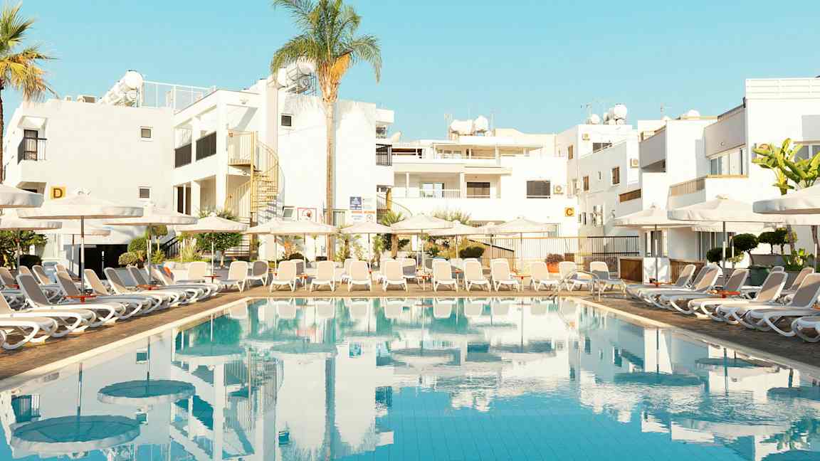 Uima-allas aurinkotuoleilla ja rakennuksia taustalla. (Tekoälyn luoma teksti)