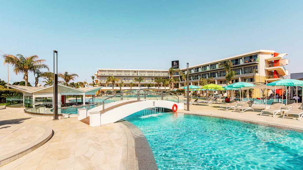 Kuva uima-altaasta, jossa on pieni silta ja hotellirakennus taustalla. (Tekoälyn luoma teksti)