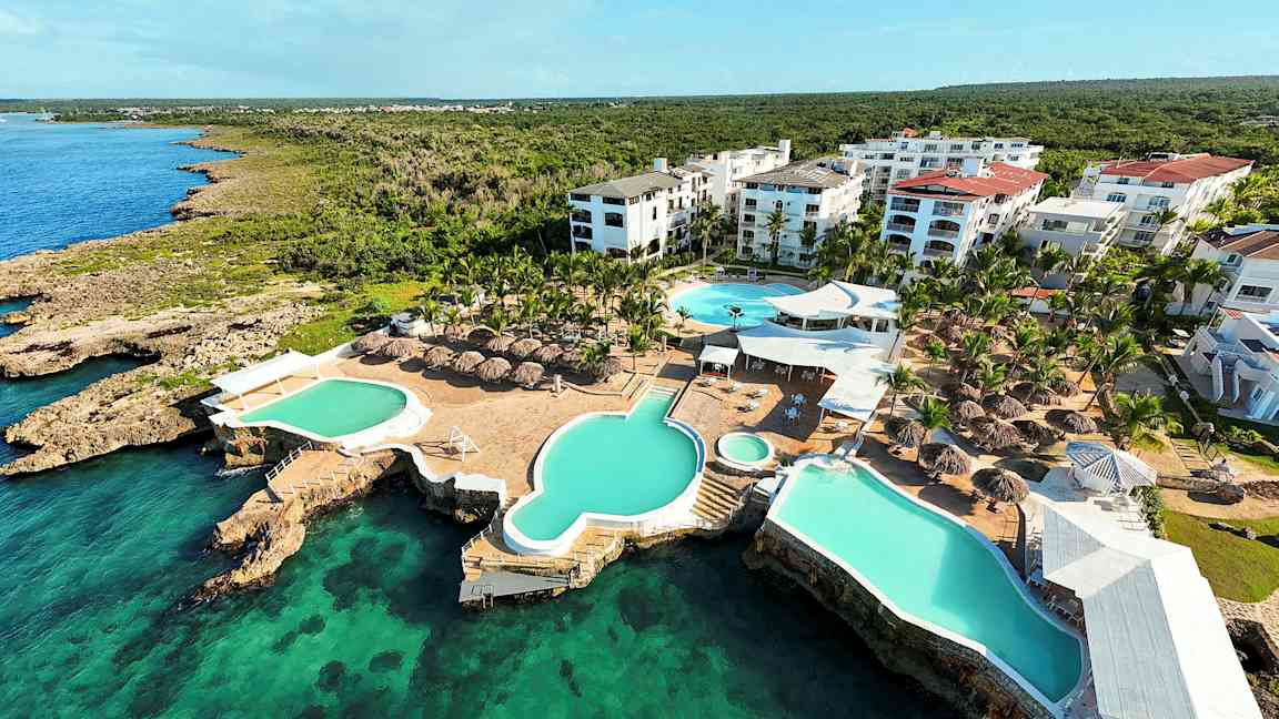 Ilmakuva lomakeskuksesta, jossa on uima-altaita ja varjokatteita meren äärellä. (Tekoälyn luoma teksti)