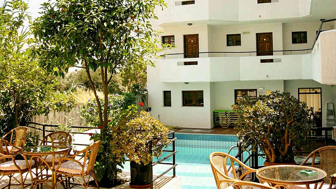 Ulkouima-allas, jota ympäröivät kasvillisuus ja istuimet, taustalla valkoinen rakennus parvekkeineen. (Tekoälyn luoma teksti)