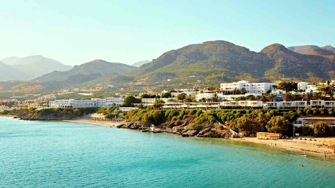 Useita rakennuksia lähellä rannikkoa, jossa on sininen meri ja vuoria taustalla. (Tekoälyn luoma teksti)