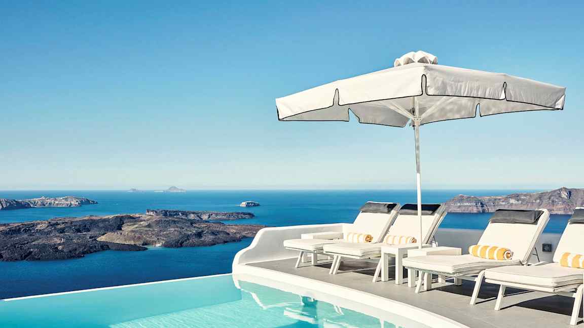 Aurinkoterassi infinity-altaan reunalla, taustalla meri ja kallioita. (Tekoälyn luoma teksti)