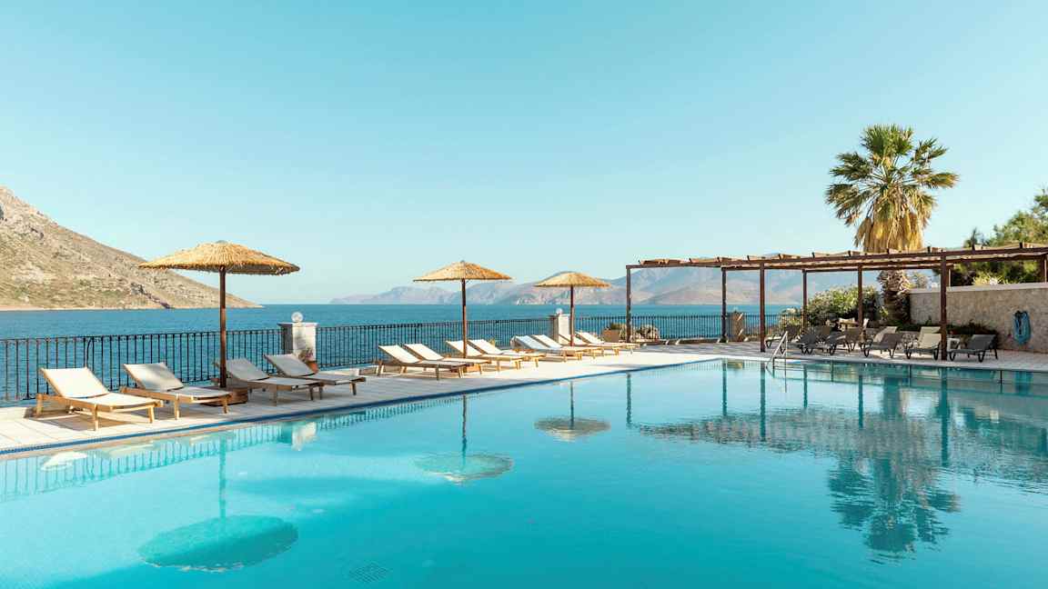 Ulkoallas aurinkotuoleilla ja aurinkovarjoilla vieressä, taustalla merimaisema. (Tekoälyn luoma teksti)