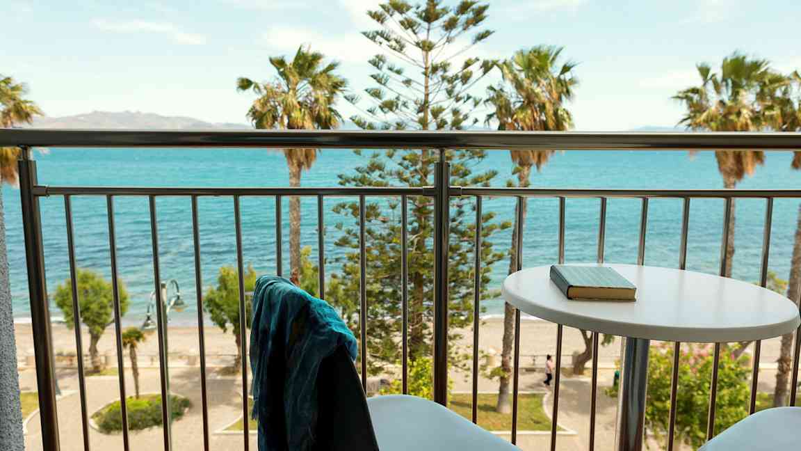 Näköala parvekkeelta pöydän ja tuolien ääressä meri ja palmuja näkyvissä. (Tekoälyn luoma teksti)