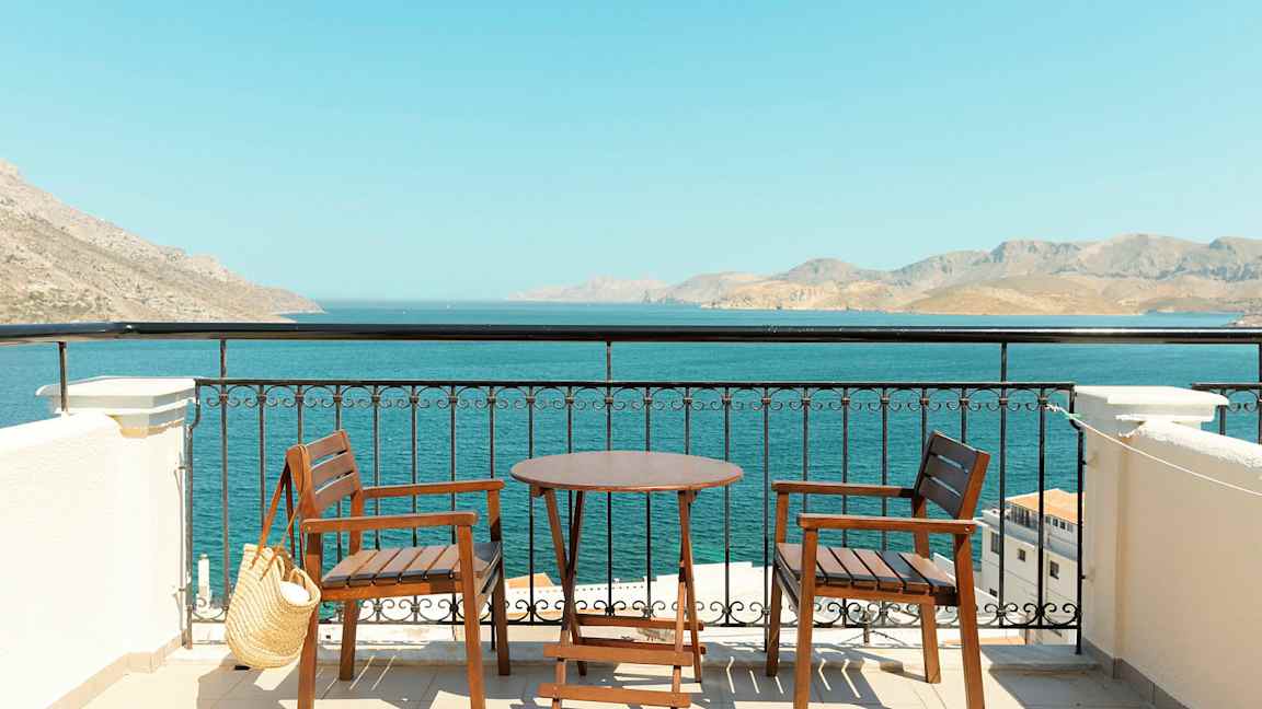 Kaksi puutuolia ja pöytä terassilla, jolta avautuu näkymä merelle ja vuoristoon kaukaisuudessa. (Tekoälyn luoma teksti)