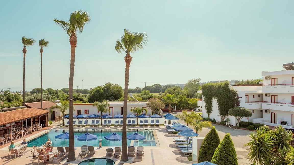 Uima-allas aurinkotuoleineen ja aurinkovarjoineen rakennusten ja puiden ympäröimänä. (Tekoälyn luoma teksti)