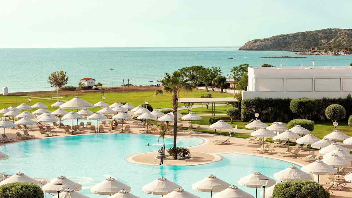 Uima-allas, jossa aurinkotuoleja ja varjoja, näkymät merelle ja vehreään ympäristöön. (Tekoälyn luoma teksti)