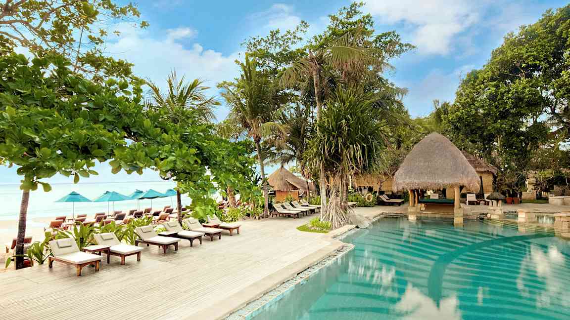 Ulkouima-allas, jota ympäröivät aurinkotuolit, aurinkovarjot ja vehreys meren rannalla. (Tekoälyn luoma teksti)