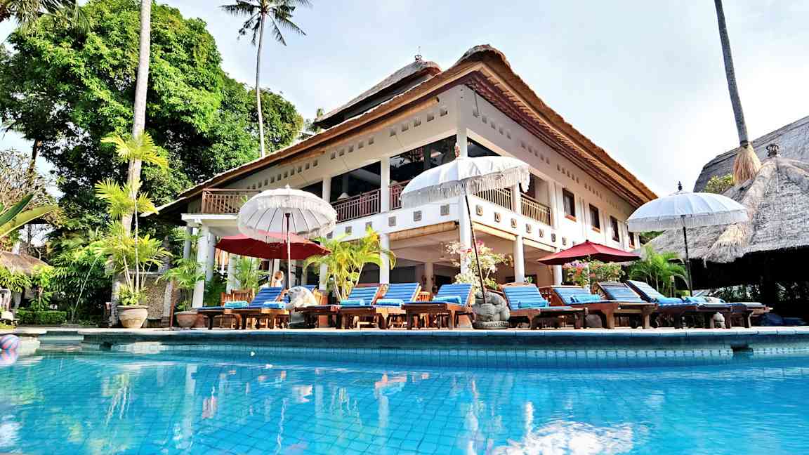 Iso huvila olkikatolla ja uima-allas edessä, ympärillä aurinkotuoleja ja varjoja. (Tekoälyn luoma teksti)