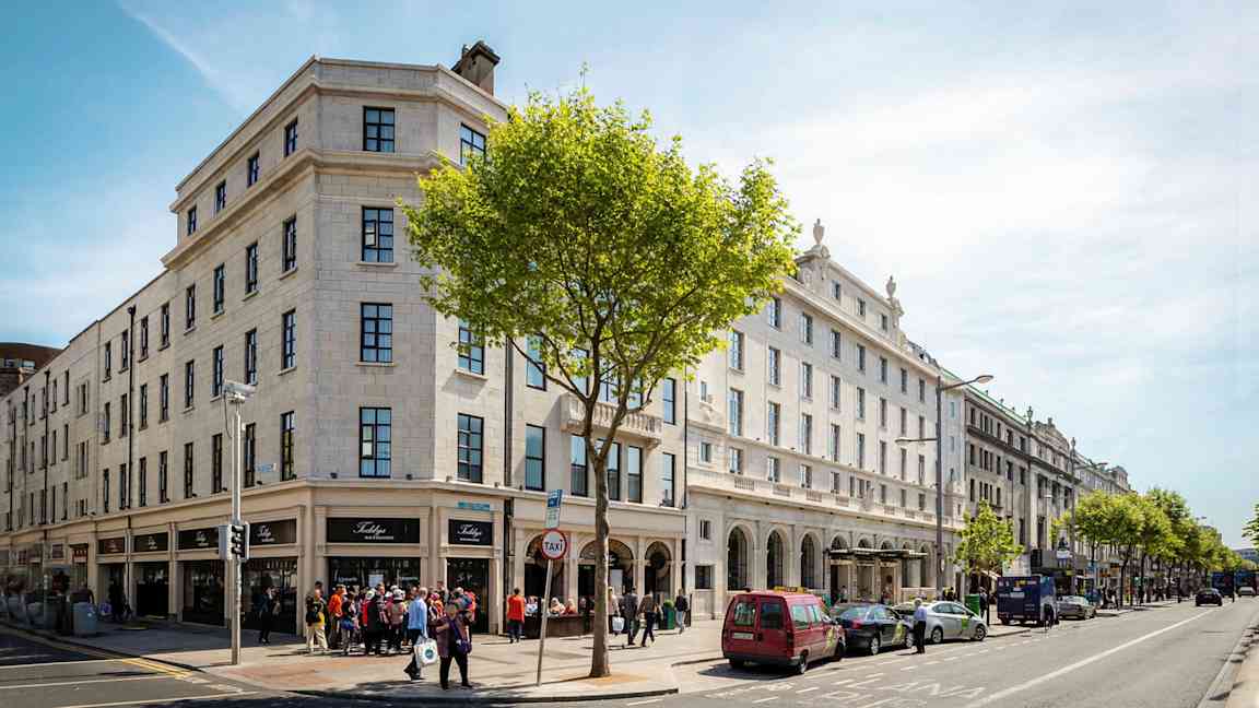 Katunäkymä rakennuksilla, pysäköidyillä autoilla ja ihmisillä. (Tekoälyn luoma teksti)