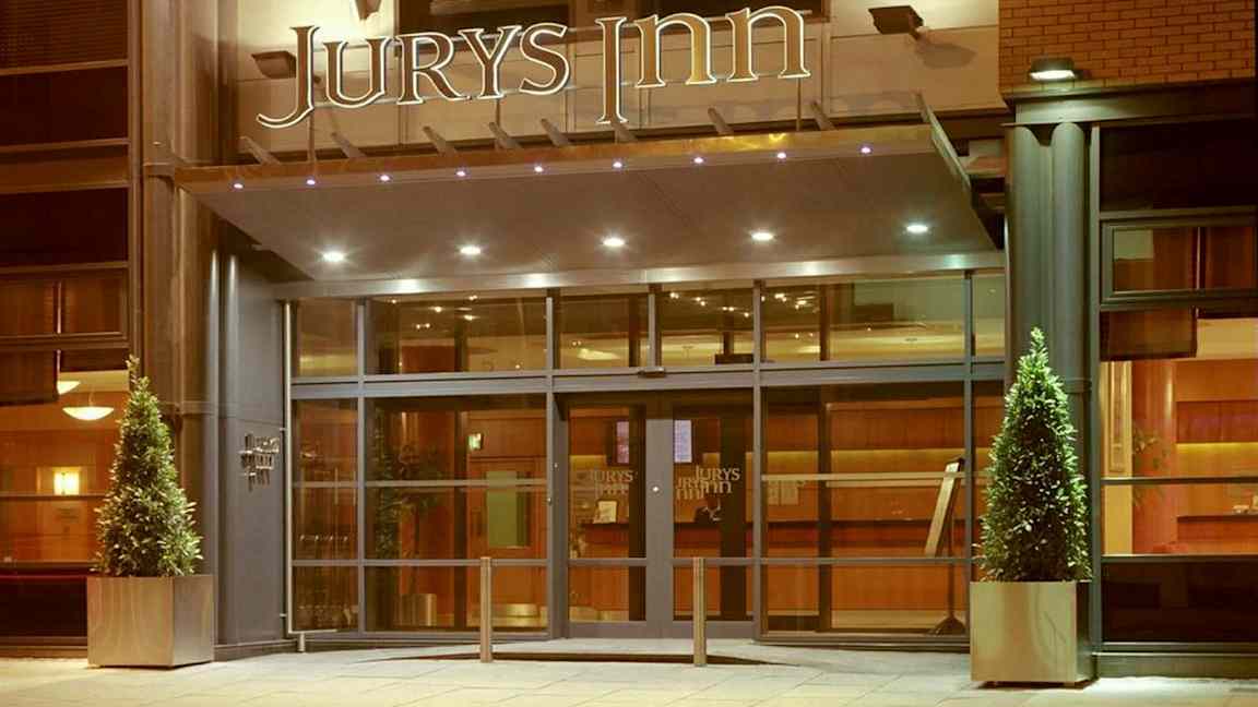 Hotellin sisäänkäynti, jossa lasiovet ja yläpuolella 'Jurys Inn' -kyltti. (Tekoälyn luoma teksti)