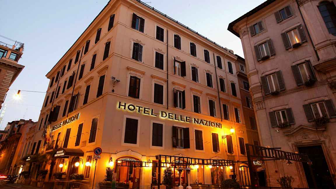 Kuva rakennuksesta, jossa kyltti, joka sanoo Hotel Delle Nazioni, valaistu iltavalaistuksella. (Tekoälyn luoma teksti)