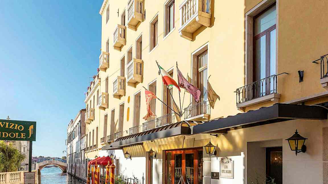 Keltainen rakennus, jossa on parvekkeita kanavan varrella, ja taustalla kävelysilta. (Tekoälyn luoma teksti)