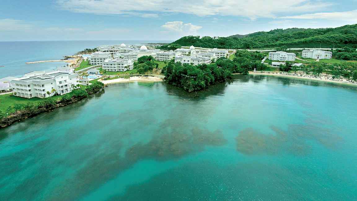 Kuva rannikon kirkkaasta vedestä ja valkoisista rakennuksista, joita ympäröi vihreä luonto. (Tekoälyn luoma teksti)