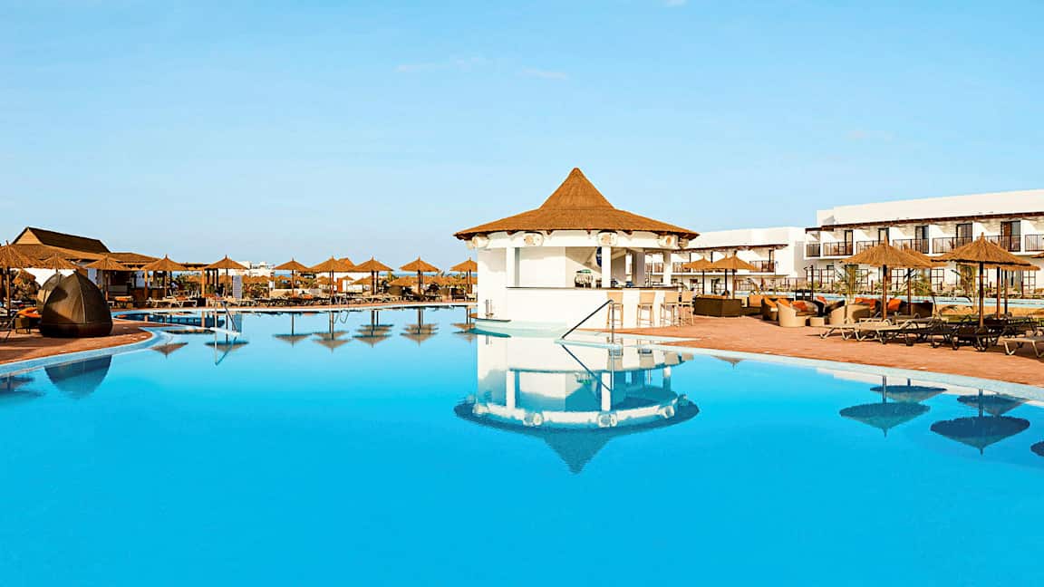 Suuri uima-allas, jossa on aurinkovarjoja ja istumapaikkoja hotellialueella. (Tekoälyn luoma teksti)