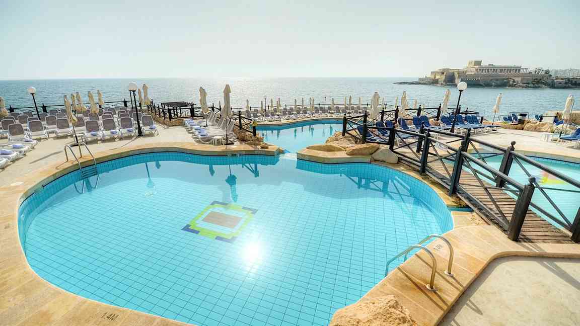 Kuva ulkouima-altaasta rannalla, ympärillä aurinkotuoleja ja aurinkovarjoja. (Tekoälyn luoma teksti)