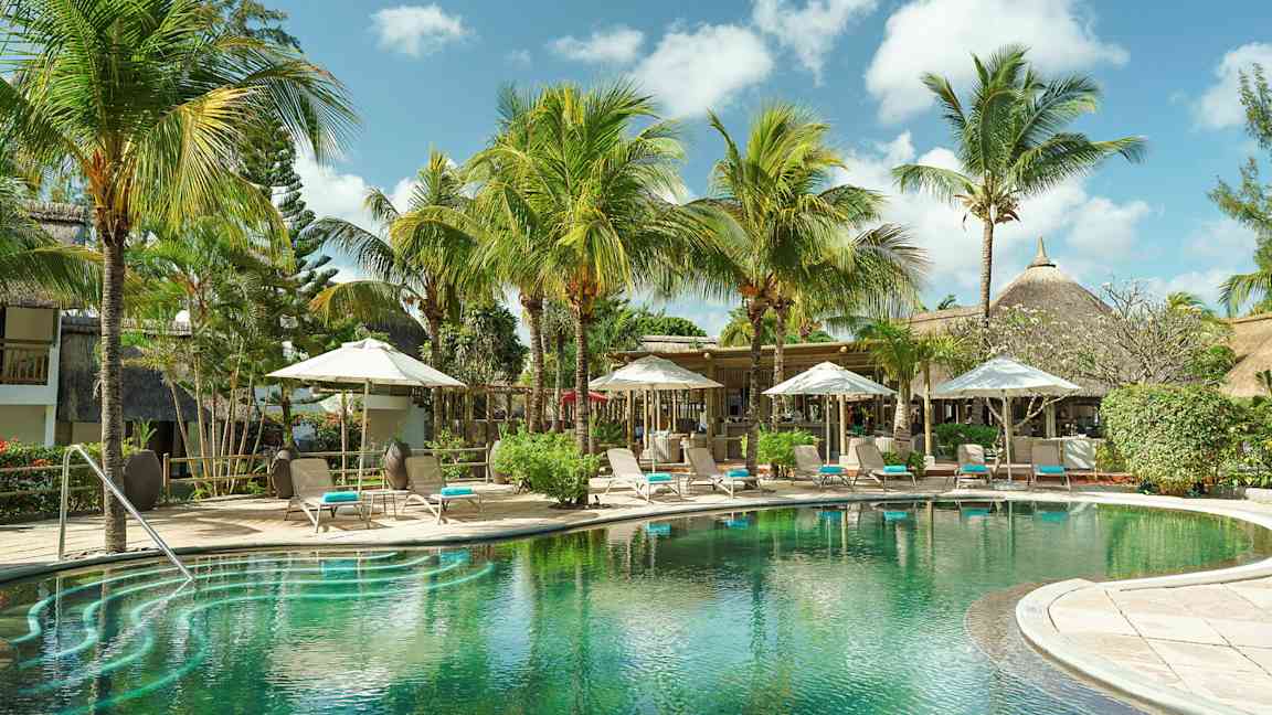 Eksoottinen uima-allas, ympärillä palmuja ja aurinkotuoleja varjojen alla. (Tekoälyn luoma teksti)