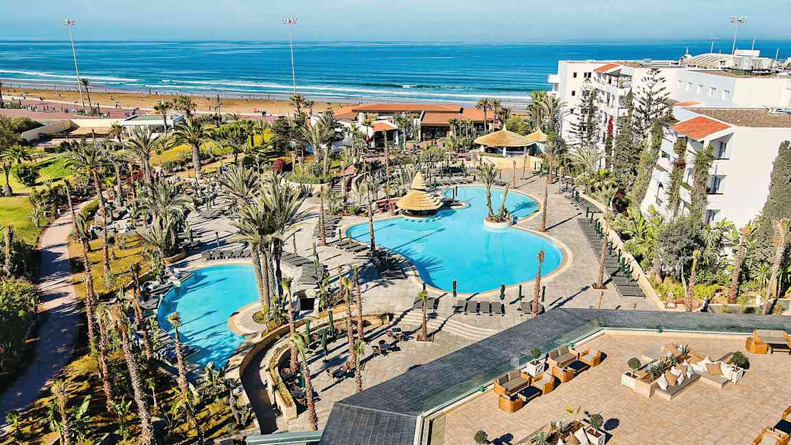 Hotellialue, jossa uima-altaita ja ympäröivää puutarhaa, sijaitsee lähellä hiekkarantaa ja merta. (Tekoälyn luoma teksti)