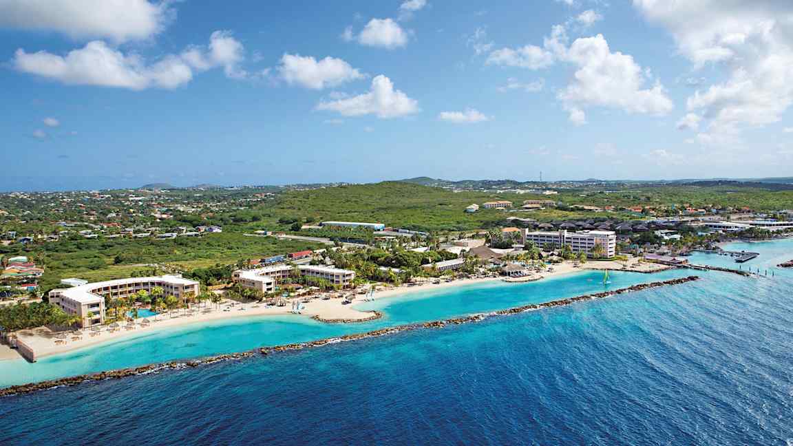 Ilmakuva rannikosta, jolla on hotellirakennuksia rannalla ja vehreyttä taustalla. (Tekoälyn luoma teksti)