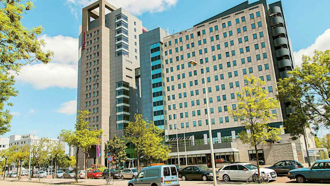 Nykyaikainen monikerroksinen rakennus, jota ympäröivät pysäköidyt autot ja puut. (Tekoälyn luoma teksti)