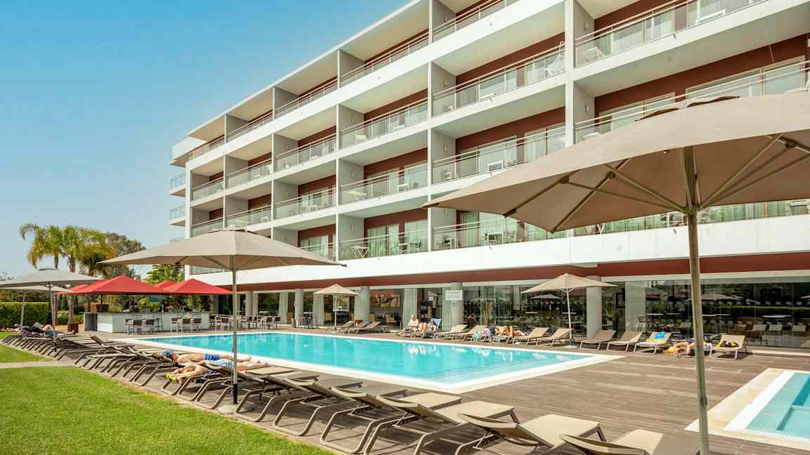 Hotellirakennus, jossa uima-allas ja aurinkotuoleja. (Tekoälyn luoma teksti)