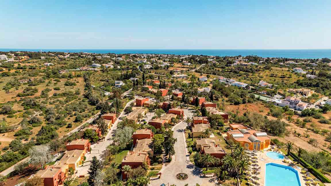 Ilmakuva lomakeskuksesta, jossa on huviloita ja uima-altaita viheralueiden ympäröimänä. (Tekoälyn luoma teksti)