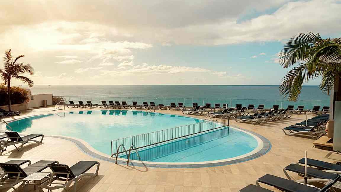 Ulkoallas aurinkotuolien ympäröimänä, sijaitsee meren lähellä kirkkaan taivaan alla. (Tekoälyn luoma teksti)