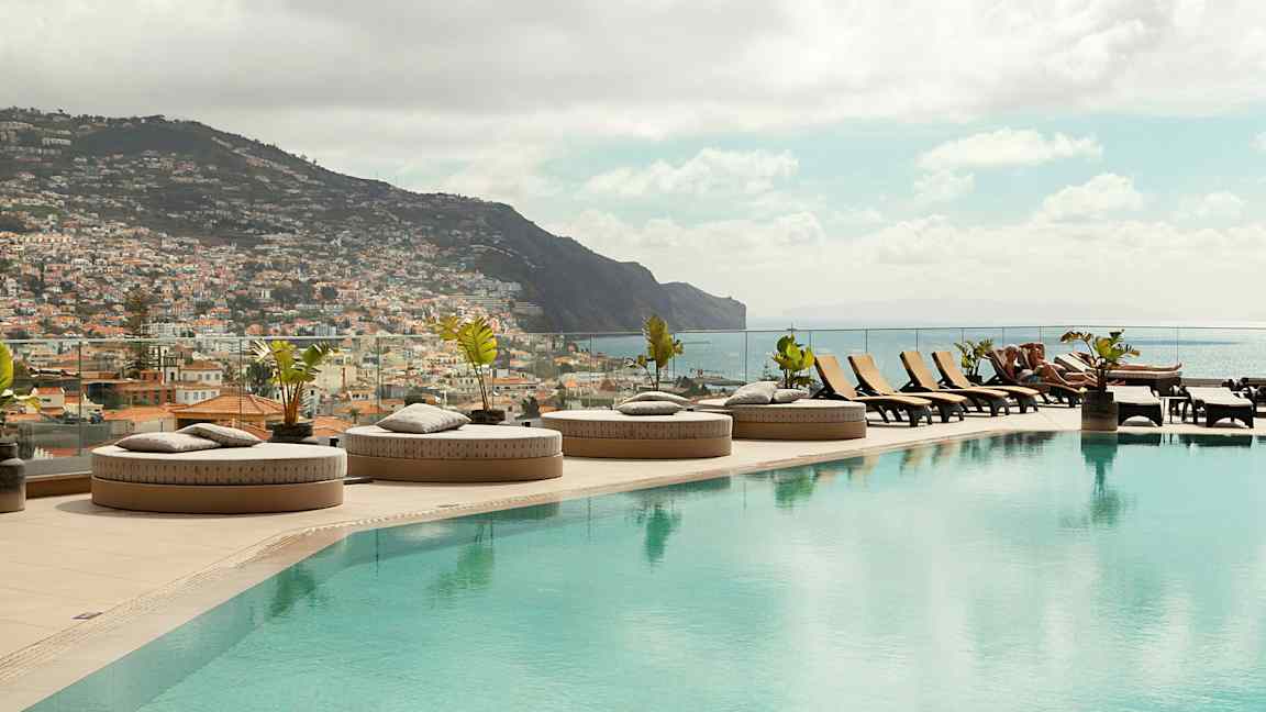 Infinity-allas, jossa aurinkotuoleja ja näkymä kaupunkiin ja vuorille. (Tekoälyn luoma teksti)