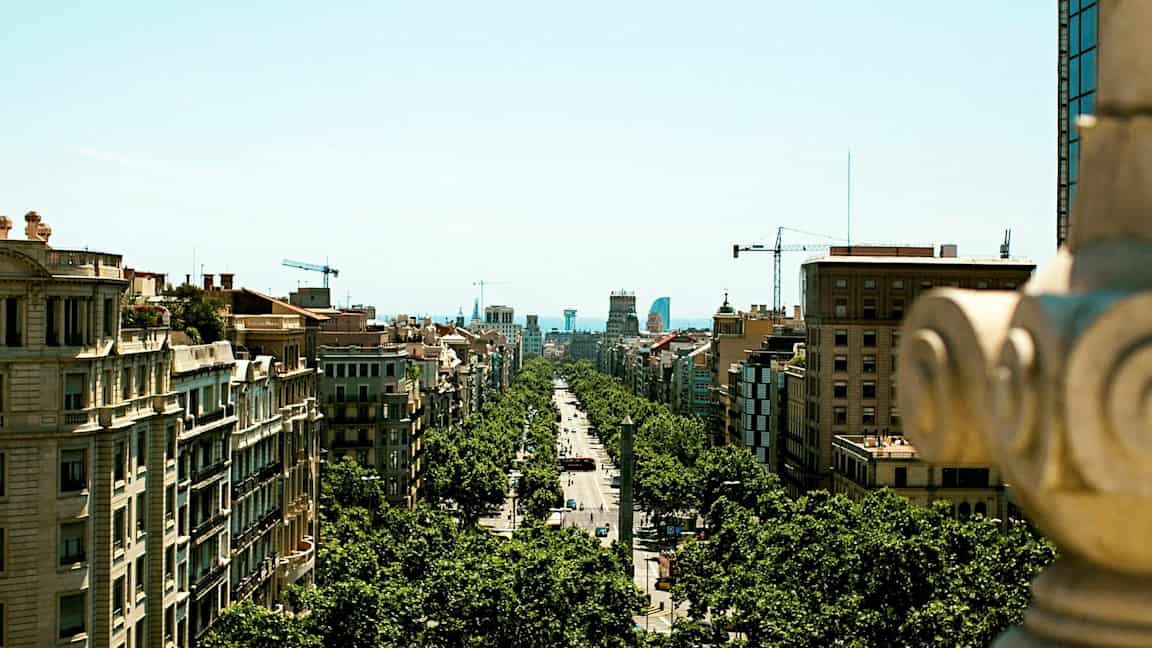 Näkymä kaupunkikadulle, joka on puiden reunustama ja rakennusten ympäröimä, kuvattuna korkeammalta paikalta. (Tekoälyn luoma teksti)