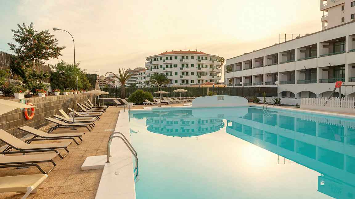 Näkymä altaalle, jossa on aurinkotuoleja vieressä ja ympäröiviä rakennuksia. (Tekoälyn luoma teksti)